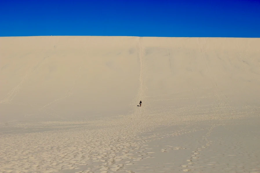 Person walking up a giant sand dune on a gorgeous blue sky day at Moreton Island in Queensland.